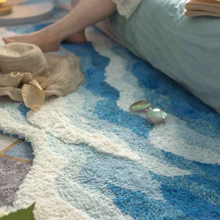 Soft blue and white area rug by Rovelli with hat and sunglasses beside a bed