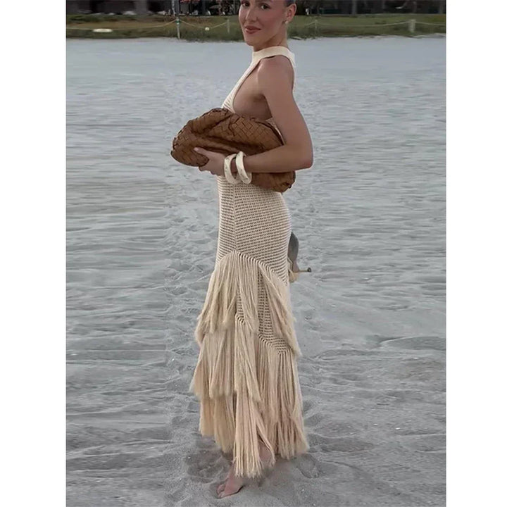 Woman in beige crochet fringe dress holding woven clutch on sandy beach, Rovelli fashion