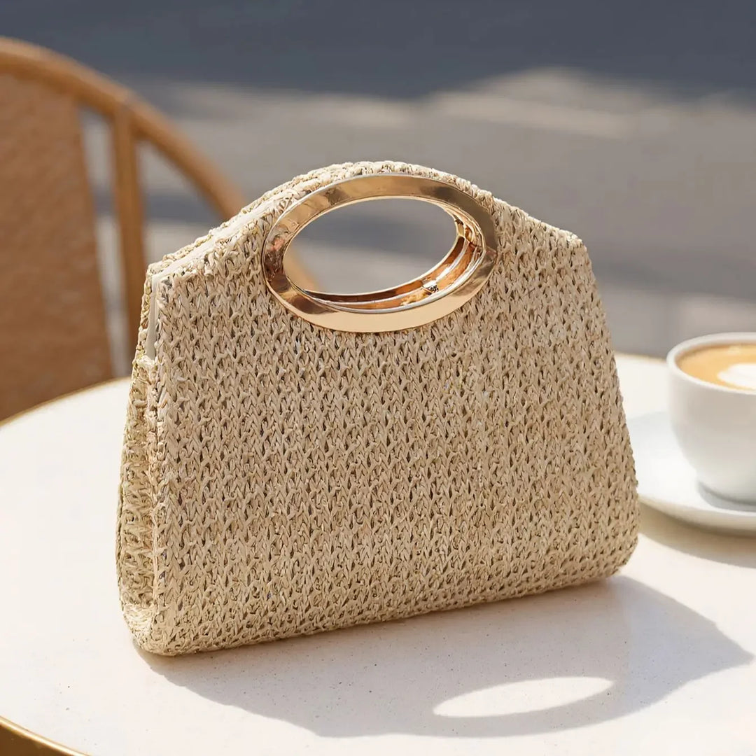 Rovelli straw handbag with gold oval handle on outdoor cafe table beside cappuccino