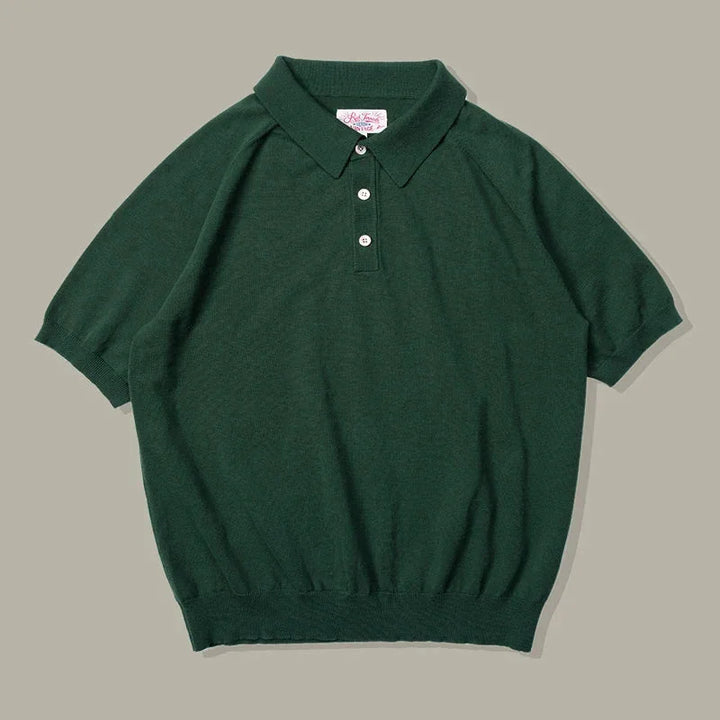 A short-sleeve, dark green classic style polo shirt with a collar, three white buttons, and ribbed cuffs and hem, laid flat on a neutral background.