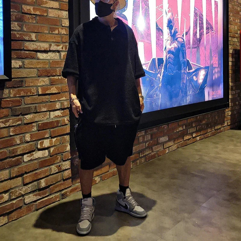 Man in black outfit and mask stands by Batman movie poster against brick wall at Rovelli