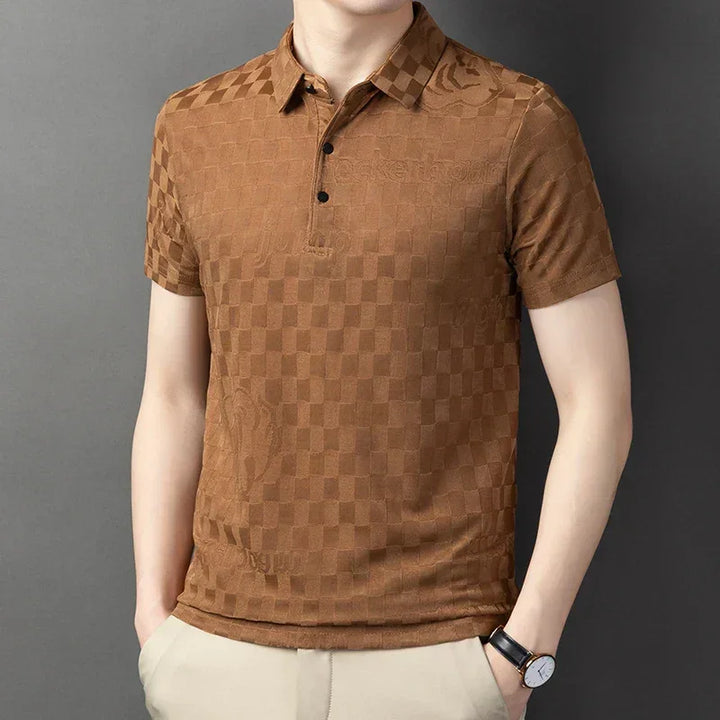 A person wearing a tailored fit, short-sleeve, brown checkerboard pattern polo shirt with a collar and three buttons, paired with light beige pants and a black watch, standing against a plain gray background.