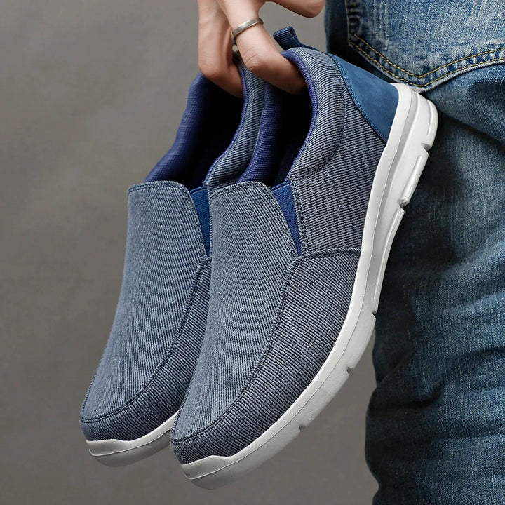 Rovelli casual blue slip-on shoes with white soles, held by a person in jeans