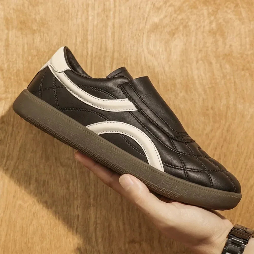 Brown leather Rovelli sneaker with white accents held against wood background
