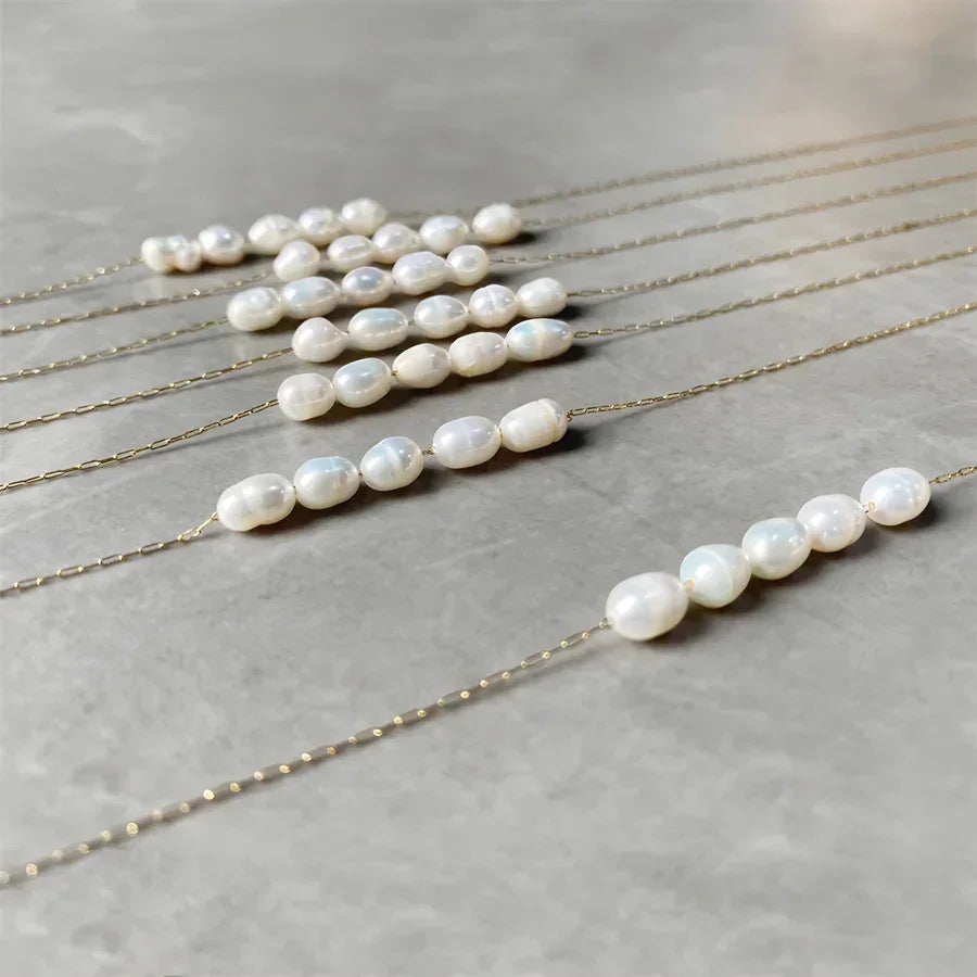 Rovelli gold chain necklaces with white freshwater pearls on a gray stone surface