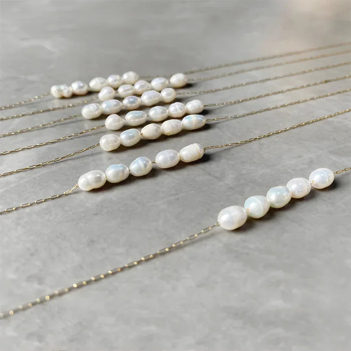Rovelli gold chain necklaces with white freshwater pearls on a gray stone surface