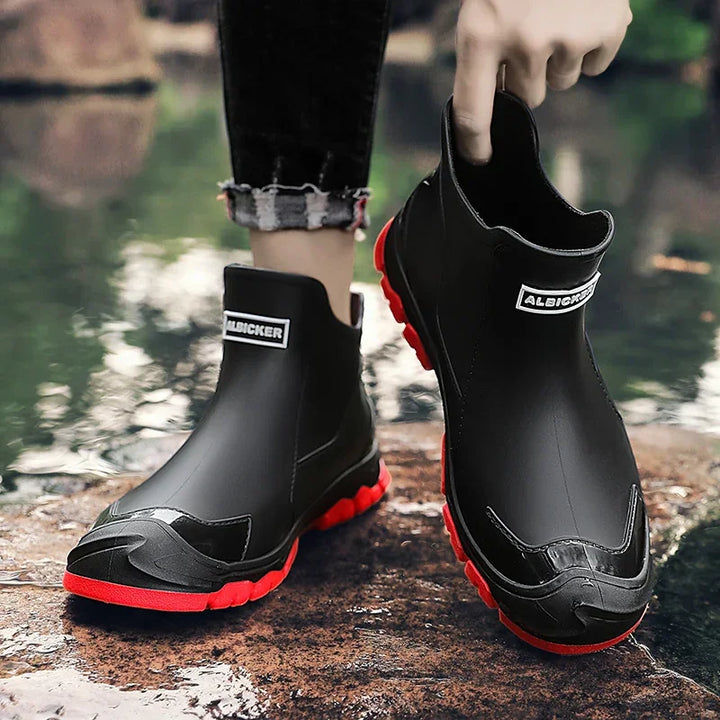 Black waterproof ankle boots with red soles worn outdoors by a river, Rovelli footwear