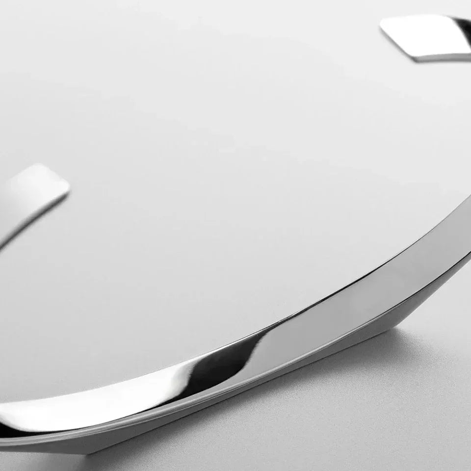 Close-up of a sleek, silver metallic arc on a smooth, light grey surface, possibly part of a modern minimalist watch face or a stainless steel bracelet. The surface has a clean and reflective finish.