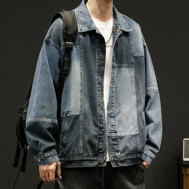 A person wearing an oversized fit, denim patchwork jacket over a white t-shirt, with black jeans and a black backpack, stands against a dark background for a retro style look.