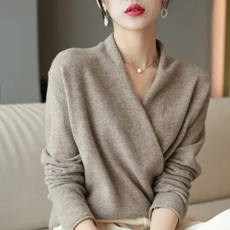 Woman wearing soft beige wrap sweater, minimalist necklace, and earrings on sofa, Rovelli fashion