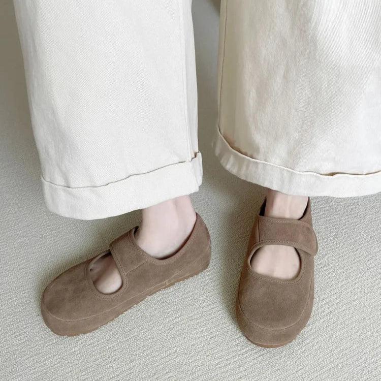 A person wearing wide-leg, light-colored pants and brown women’s casual shoes, styled as Mary Janes, stands on a light textured carpet. Only the lower legs and feet are visible in the image.