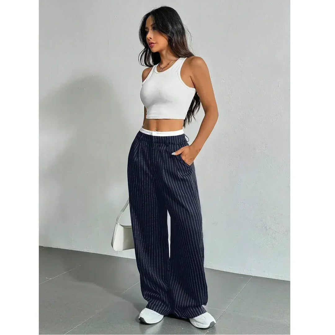 Woman wearing a white crop top and navy striped wide-leg pants, standing indoors, Rovelli fashion