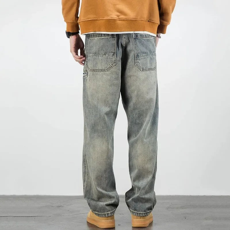 A person wearing classic fit, faded baggy jeans with two large rear pockets, a brown sweatshirt, and tan shoes stands facing away, showcasing the straight leg jeans from behind.