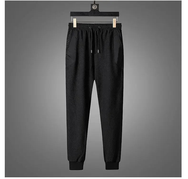 Black jogger pants with an elastic waistband, drawstring, and cuffed ankles, part of an activewear set, displayed hanging on a wooden hanger against a plain gray background.