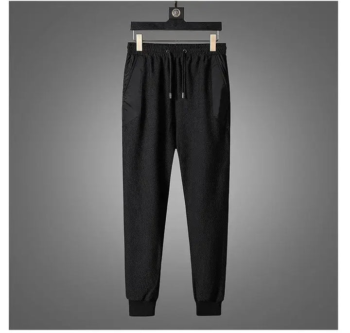 Black jogger pants with an elastic waistband, drawstring, and cuffed ankles, part of an activewear set, displayed hanging on a wooden hanger against a plain gray background.