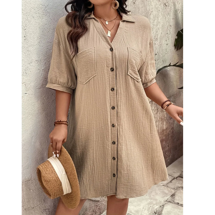Woman wearing beige button-up shirt dress with pockets, holding straw hat, Rovelli fashion