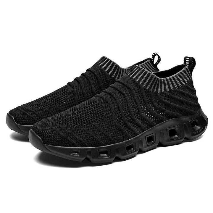 A pair of black slip-on athletic sneakers with a breathable mesh upper, ribbed texture, and a sock-like fit, featuring thick cushioned soles with square cut-out details and a handy pull tab at the heel.