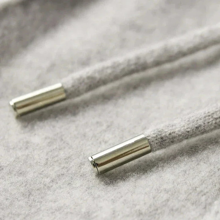 Close-up of two light gray hoodie drawstrings with shiny silver metal aglets, resting on a soft, textured gray fabric background—pair perfectly with comfortable pants for a relaxed look.