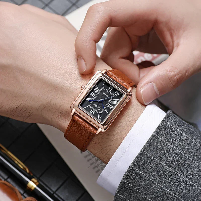 A person wearing a gray pinstripe suit adjusts a luxury watch with a rectangular gold case, a premium leather band, and a black face featuring white Roman numerals.