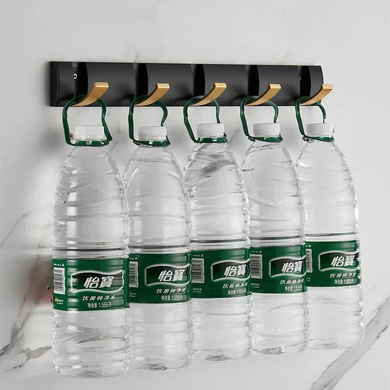 Wall-mounted black and gold hooks holding large water bottles, modern storage solution by Rovelli