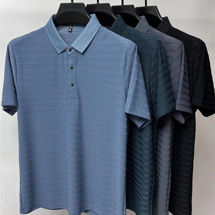 Four textured classic polo shirts in shades of blue and black are hung on black hangers, displayed in a row against a plain background, showcasing refined style and premium silk fabric.