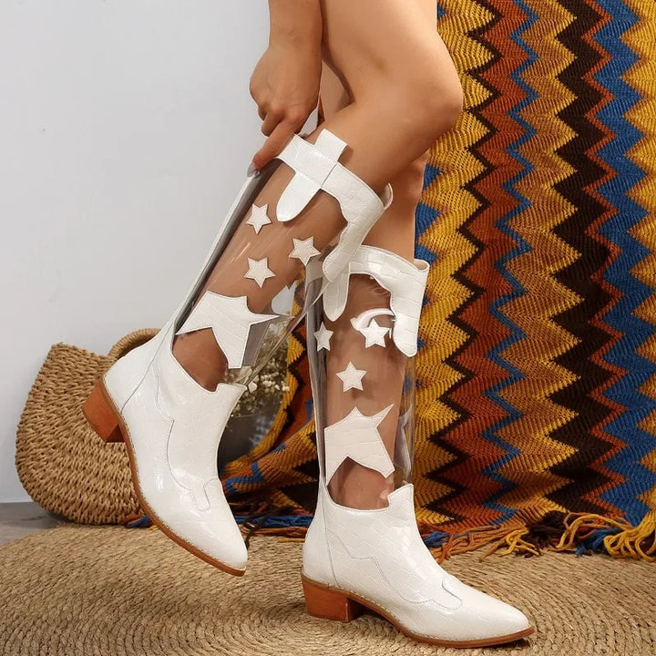 Person wearing clear panel boots with white stars and shapes, featuring white toes, heels, and light brown soles. Background includes a woven basket and a colorful zigzag patterned rug.