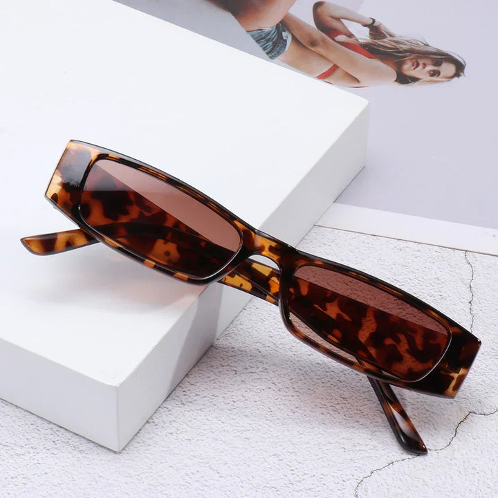 Retro rectangle sunglasses with UV400 protection and brown lenses rest on a white surface, complemented by a partial photo of a woman in a bikini visible in the background.
