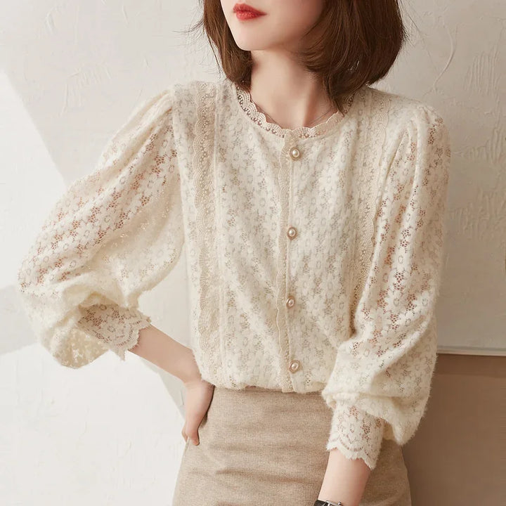 A woman wearing an ivory lace blouse with a floral lace pattern and vintage pearl buttons, paired with a beige skirt, stands against a light background.