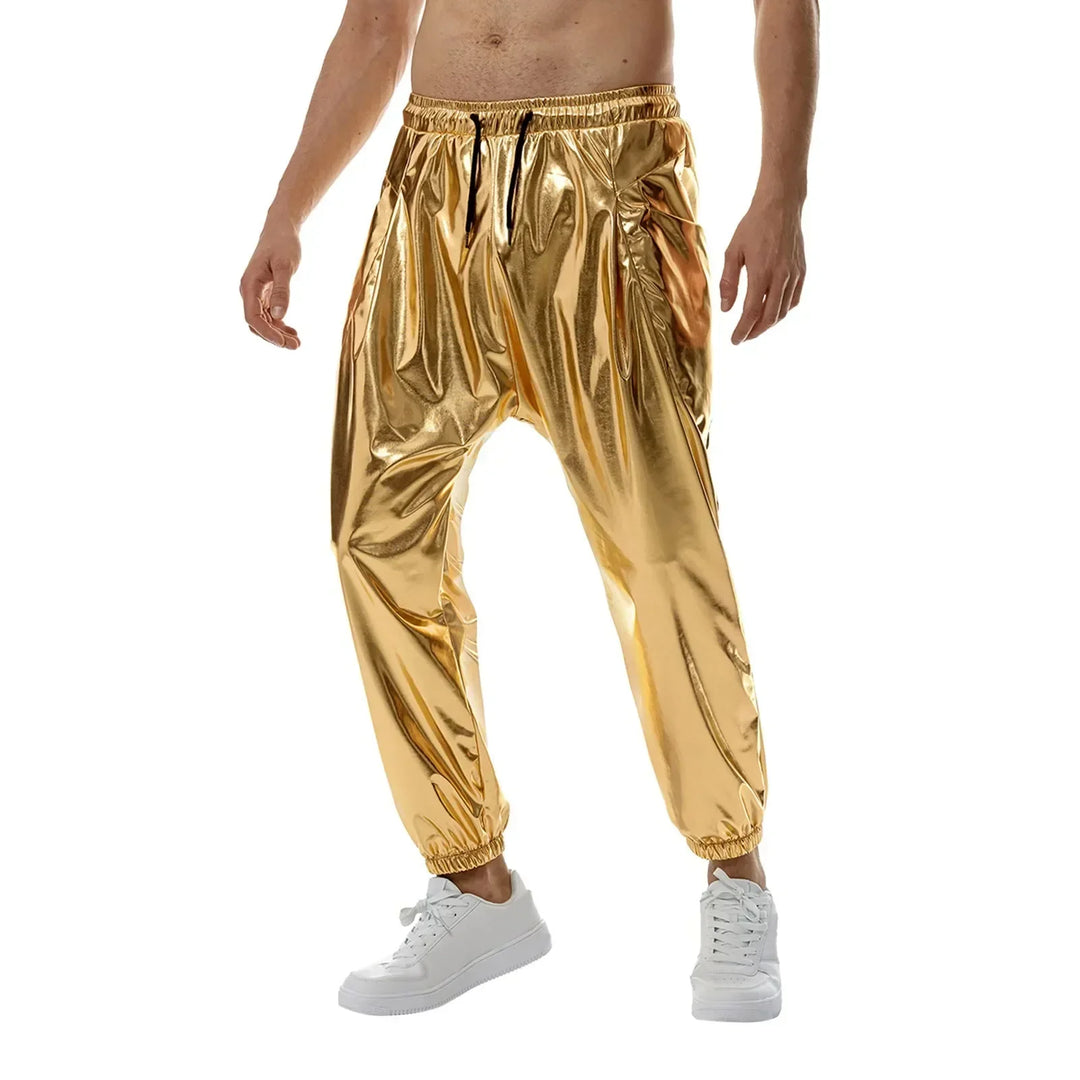 A person wears shiny gold harem pants with an elastic waistband and cuffs, made from lightweight metallic fabric, paired with white sneakers. The person is shirtless and stands against a plain white background.