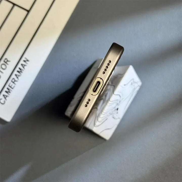 A close-up view of the bottom edge of a smartphone with a USB-C charging port and speaker grills, featuring a slim lightweight design and placed on a marble-patterned stand with a clapperboard partially visible in the background.