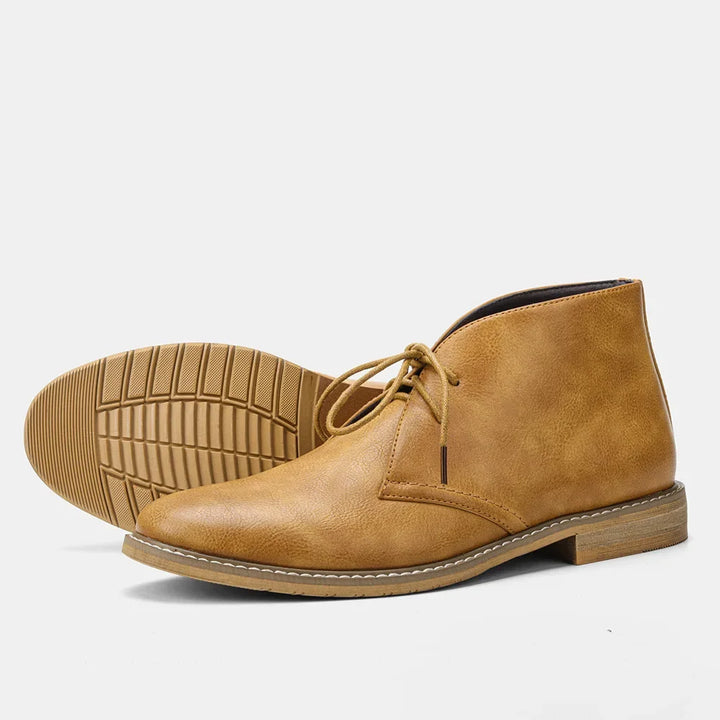A pair of tan leather After-Ride Chukka boots, one upright and one laying on its side showing the textured sole, against a plain white background.