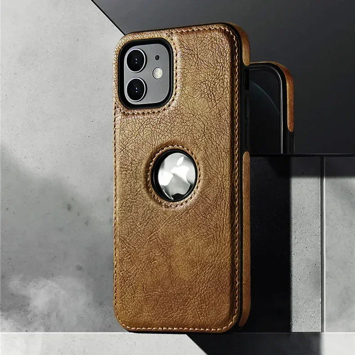 A luxury leather phone case in brown with a circular cutout reveals an Apple AirTag. This slim protective case, wireless charging compatible, props your iPhone stylishly against a gray and black tiled surface.