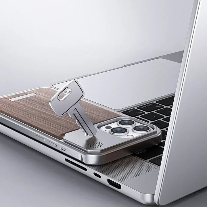 A key is inserted into a smartphone with a stylish phone case, partly tucked under a laptop, creating an illusion that the phone works like a USB drive. The devices are placed on a light gray surface.