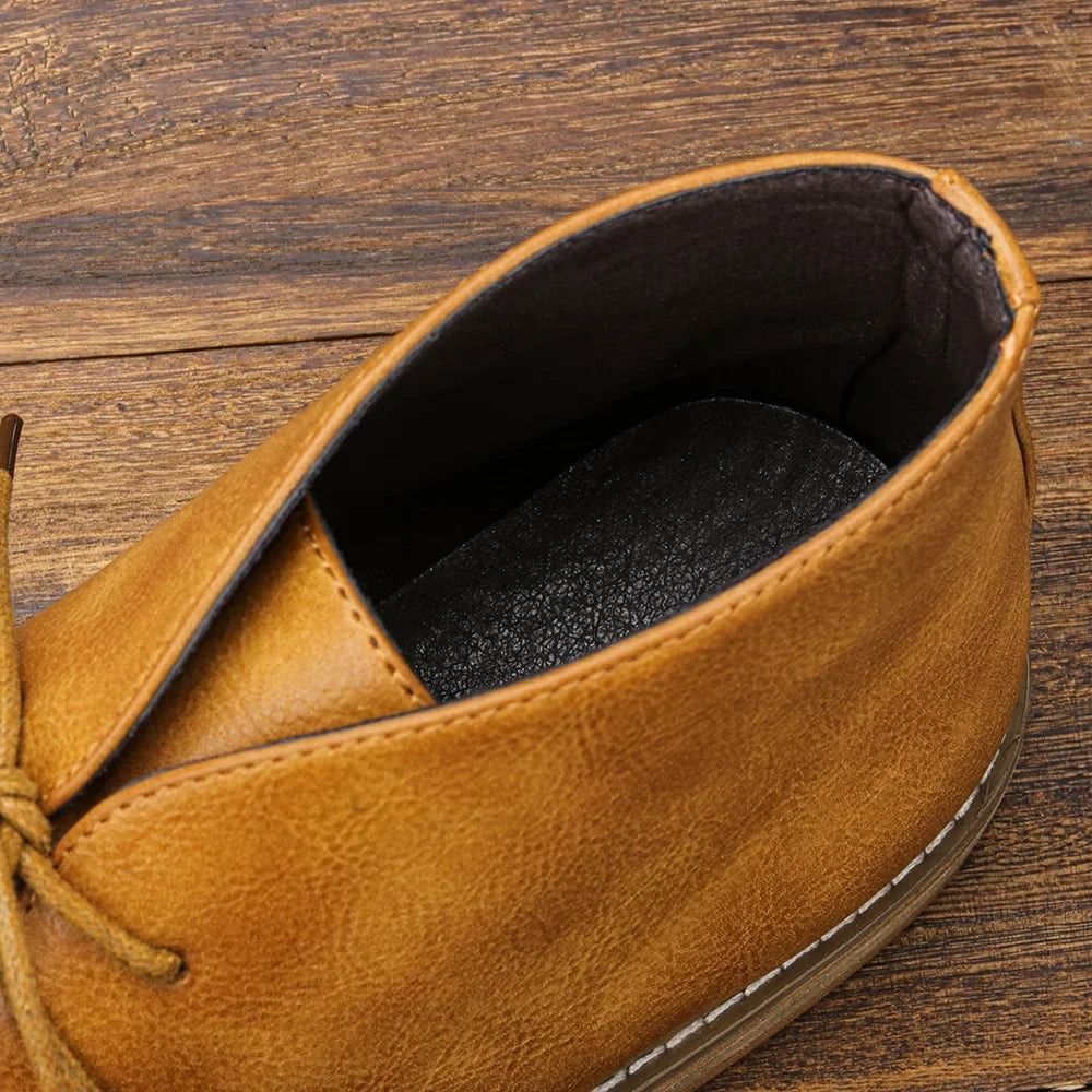 A close-up view of a tan After-Ride Chukka shoe with visible stitching and a black insole, set on a wooden surface. The shoe’s laces and upper details are clearly shown, highlighting its Western-inspired chukka design.
