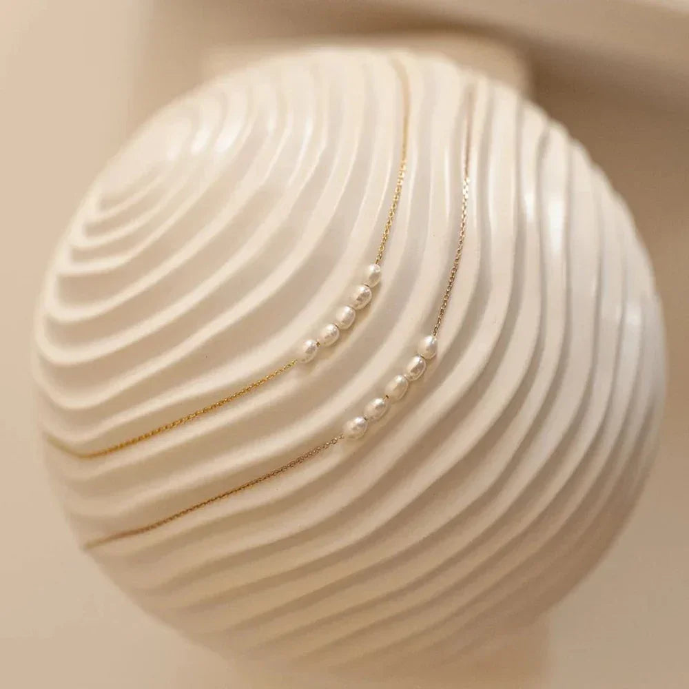 Minimalist gold chain pearl necklace on textured white ceramic vase, Rovelli jewelry