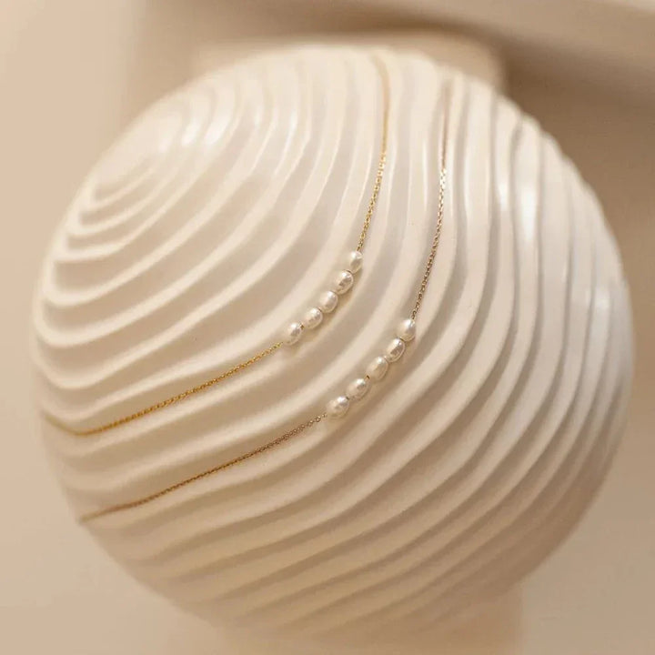 Minimalist gold chain pearl necklace on textured white ceramic vase, Rovelli jewelry