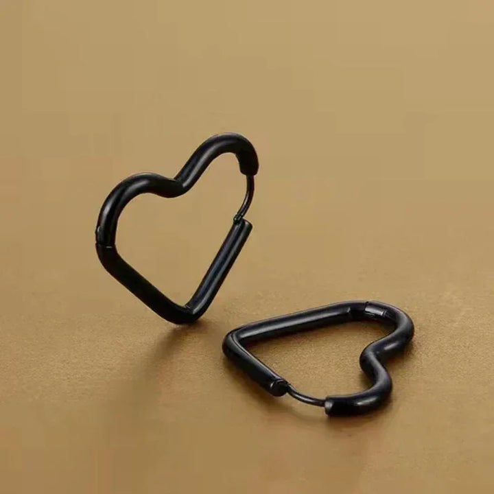 Two black heart-shaped carabiner clips, featuring minimalist design, are displayed on a plain brown surface—one standing upright and the other lying flat.
