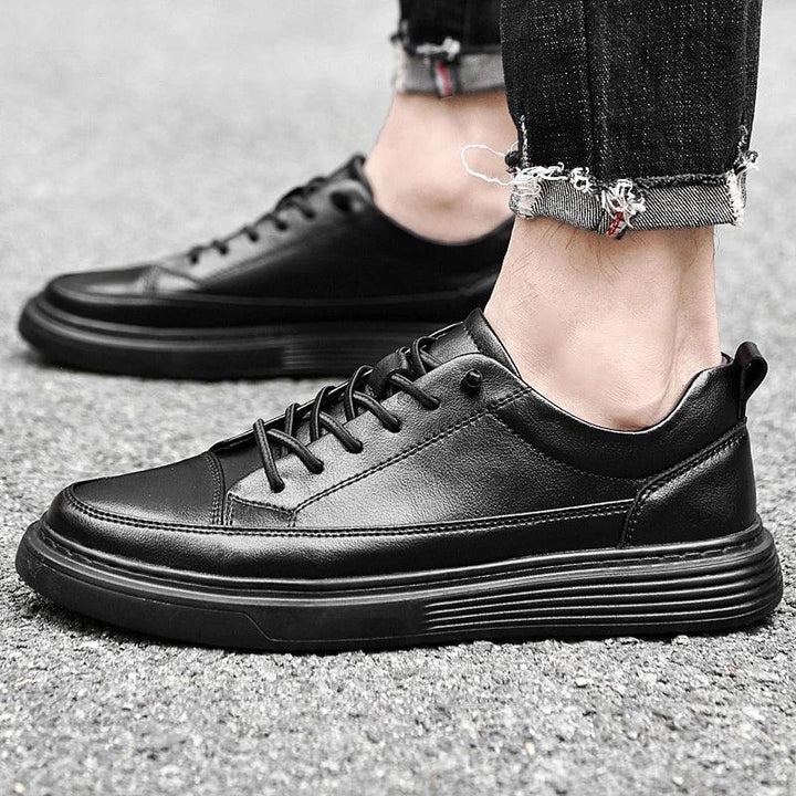 A person wearing black leather sneakers with black laces and thick black soles, enhanced by RunForm insoles, stands on a gray pavement. The look is completed with black jeans featuring frayed hems.