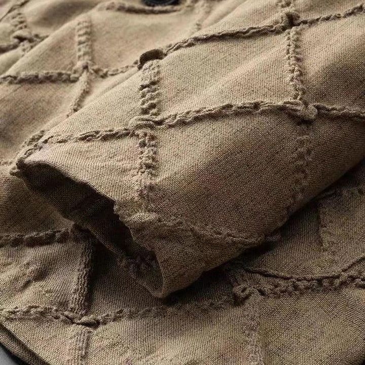 A close-up of brown fabric with a quilted diamond pattern. The stitching creates raised, grid-like diamonds across the material, and a folded section is visible in the foreground—perfect for luxury two-piece sets or relaxed fit trousers.