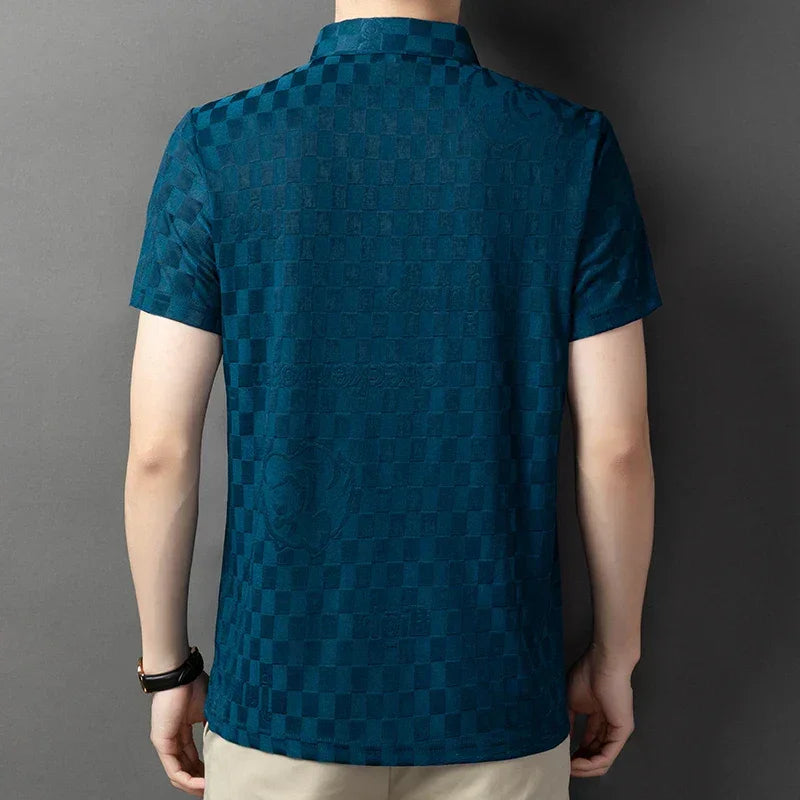 A person wearing a short-sleeve, teal checkerboard pattern polo shirt and beige pants with a tailored fit is standing with their back to the camera against a neutral background.