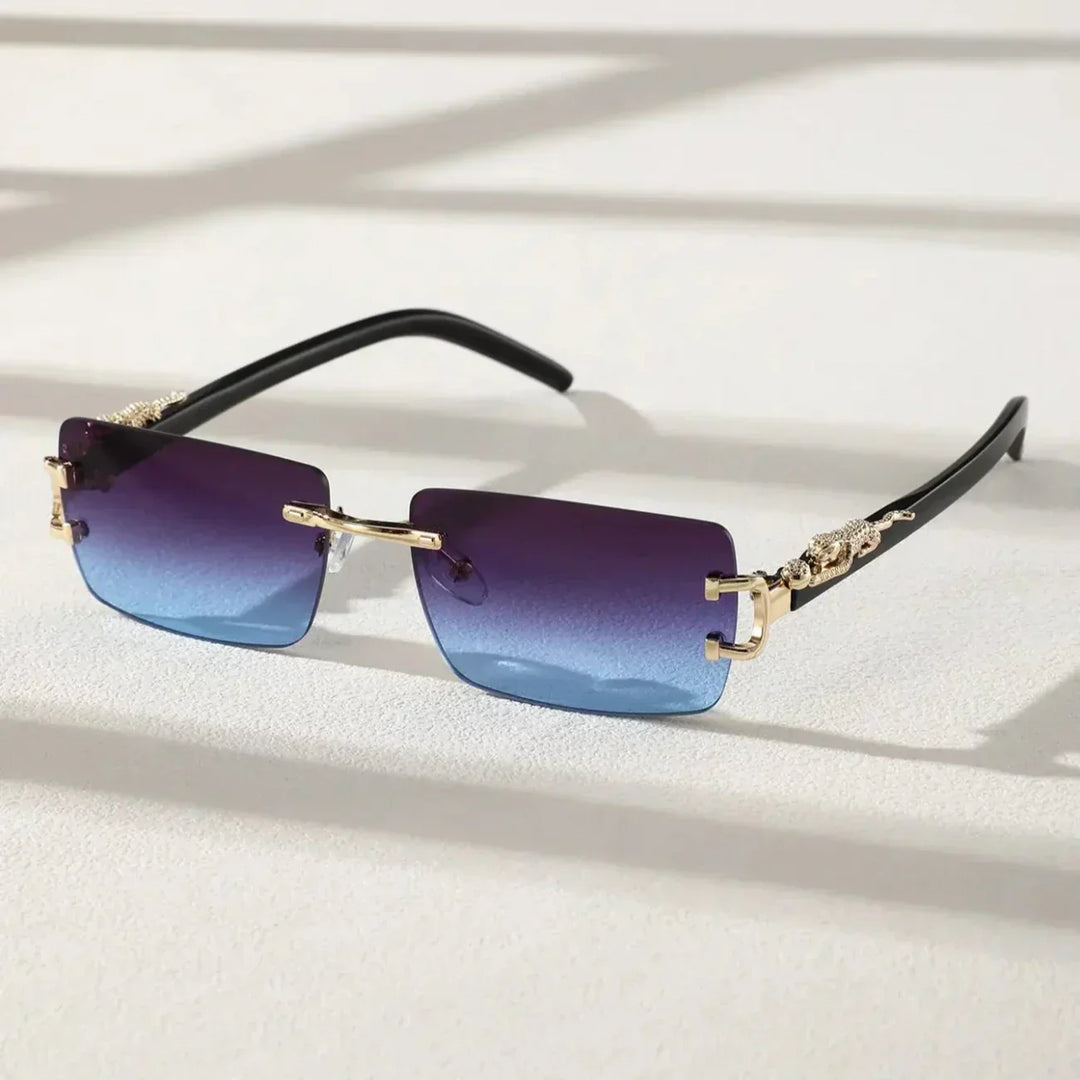 A pair of rimless, rectangular sunglasses with UV400 protection, gradient blue tint, gold decorative arms, and black temple tips, placed on a light textured surface with shadow lines.