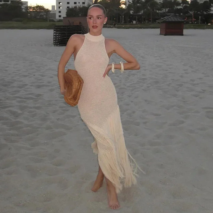 Woman on beach in cream knit fringe dress holding brown clutch, Rovelli fashion.