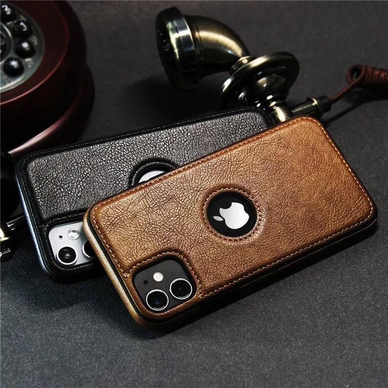 Two smartphones with luxury leather phone cases—one brown, one black—rest on a dark surface near an old-fashioned rotary telephone handset. The Apple logo is visible through circular cutouts, highlighting their slim protective case design.