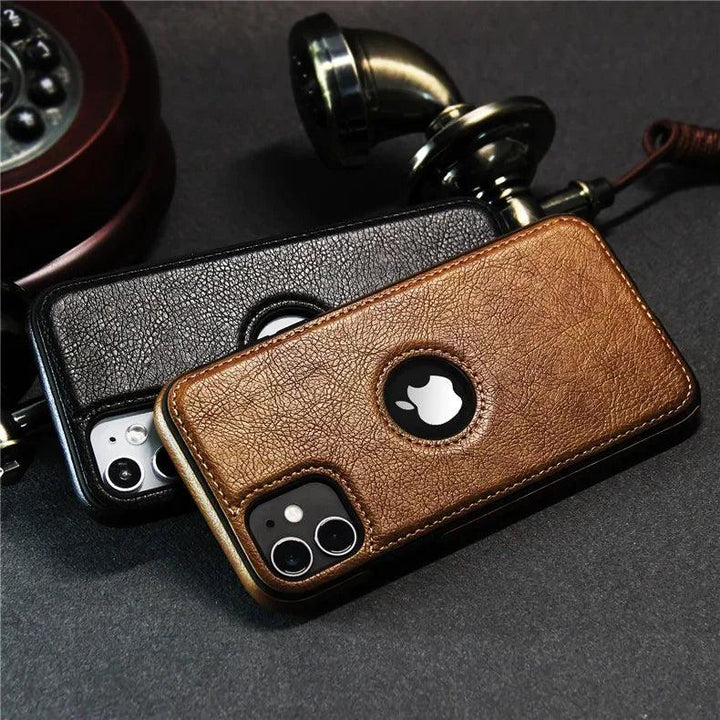 Two smartphones with luxury leather phone cases—one brown, one black—rest on a dark surface near an old-fashioned rotary telephone handset. The Apple logo is visible through circular cutouts, highlighting their slim protective case design.