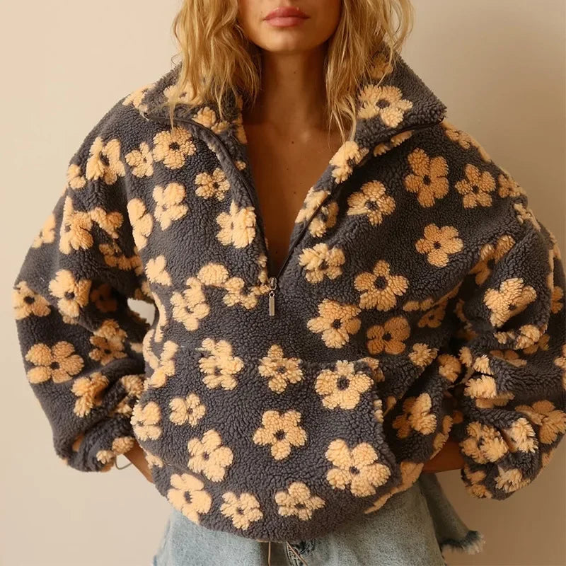 A woman wears a cozy, fuzzy gray flannel pullover with a zipper and yellow floral pattern, crafted from extra-heavy fabric, paired with light blue denim shorts. Her face is partially out of frame.
