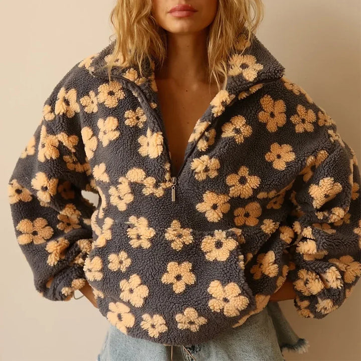 A woman wears a cozy, fuzzy gray flannel pullover with a zipper and yellow floral pattern, crafted from extra-heavy fabric, paired with light blue denim shorts. Her face is partially out of frame.