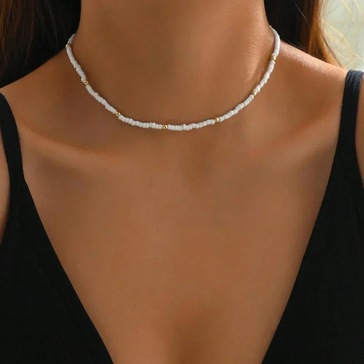Woman wearing a Rovelli white beaded choker necklace with gold accents, black top