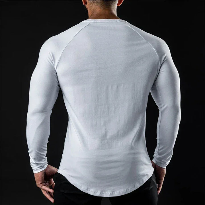 A person with a muscular build is shown from the back, wearing a fitted, moisture-wicking long sleeve shirt and black pants, standing against a black background.