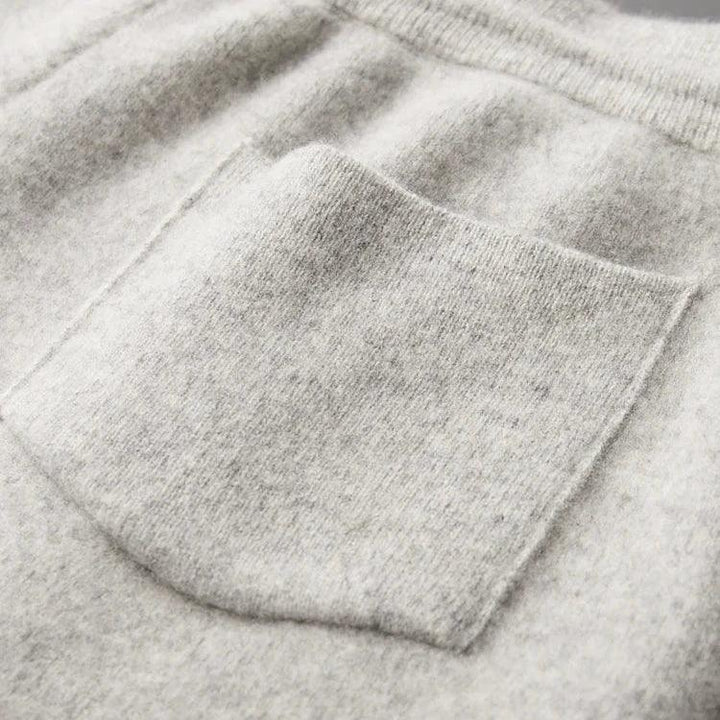 Close-up of a light grey, soft-textured sweater with a neatly sewn square pocket on the front. The fabric appears cozy and plush, with slight ribbing at the top edge and durable construction for lasting wear.