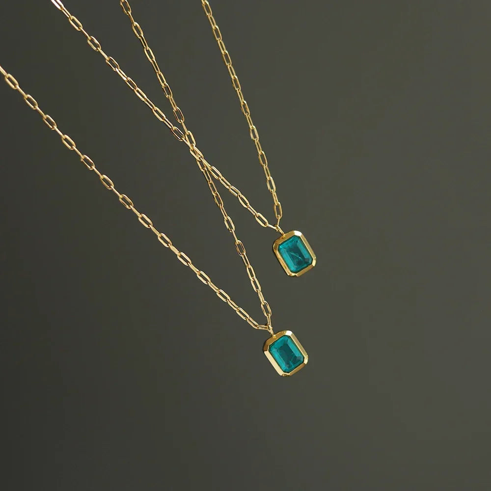 Two delicate 18K gold plated chains with rectangular green zirconia pendants are displayed against a plain dark background.